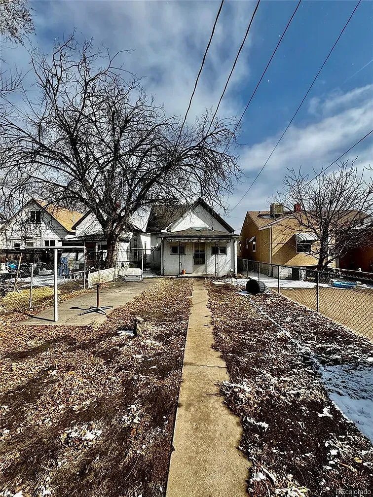 Snow-dusted front yard with a concrete path leading to a small white house under a cloudy blue sky. Snow-dusted front yard with a concrete path leading to a small white house under a cloudy blue sky.