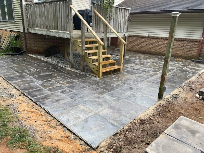 A patio with stairs leading up to a deck and a house in the background.