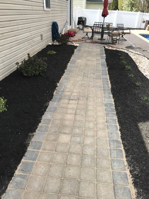 A brick walkway leading to a patio with a table and chairs.