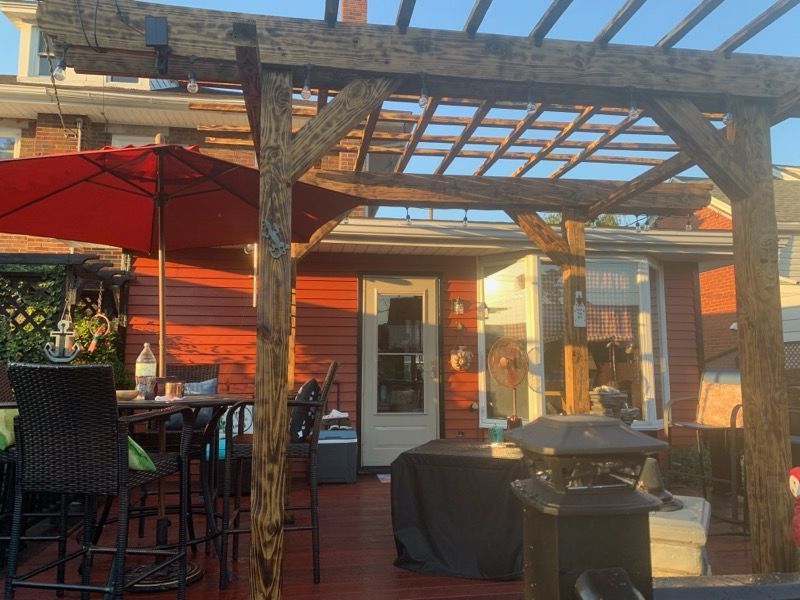 A wooden pergola is sitting on top of a patio with tables and chairs.