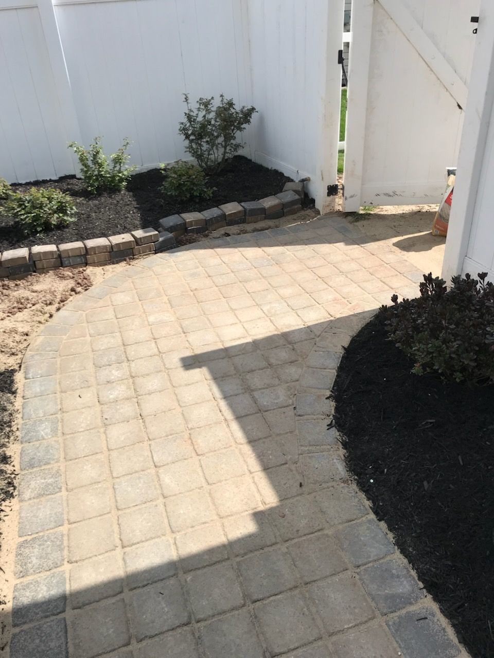 A brick walkway leading to a white house with a white fence.
