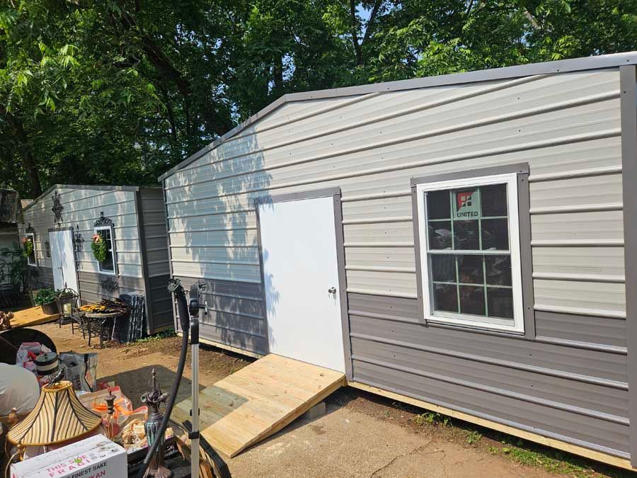 Two metal sheds with gray and white siding, one with a ramp.