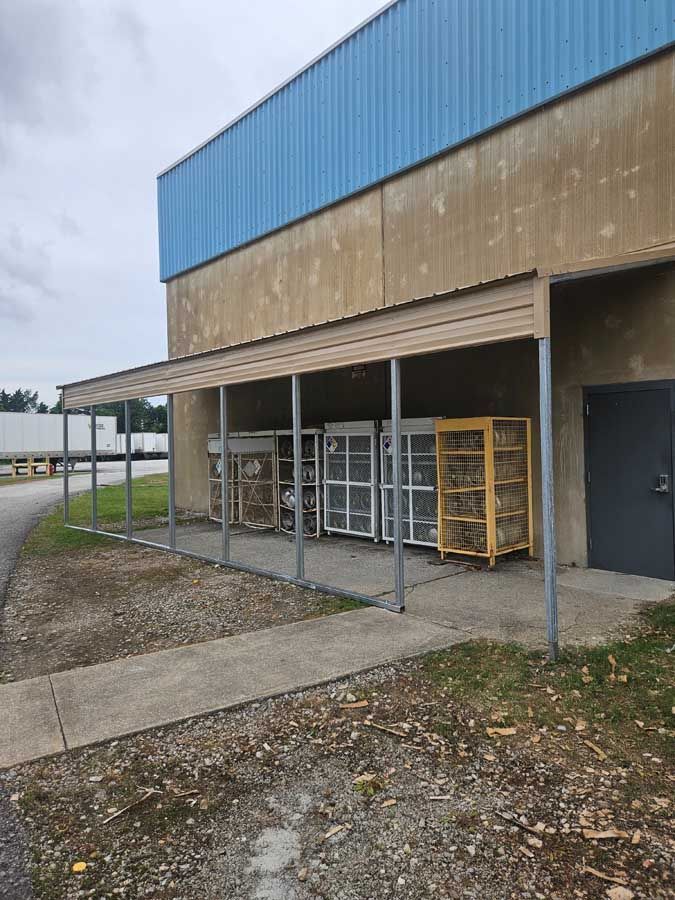 Outside a building, covered area with several metal storage cages on a concrete slab; overcast sky.