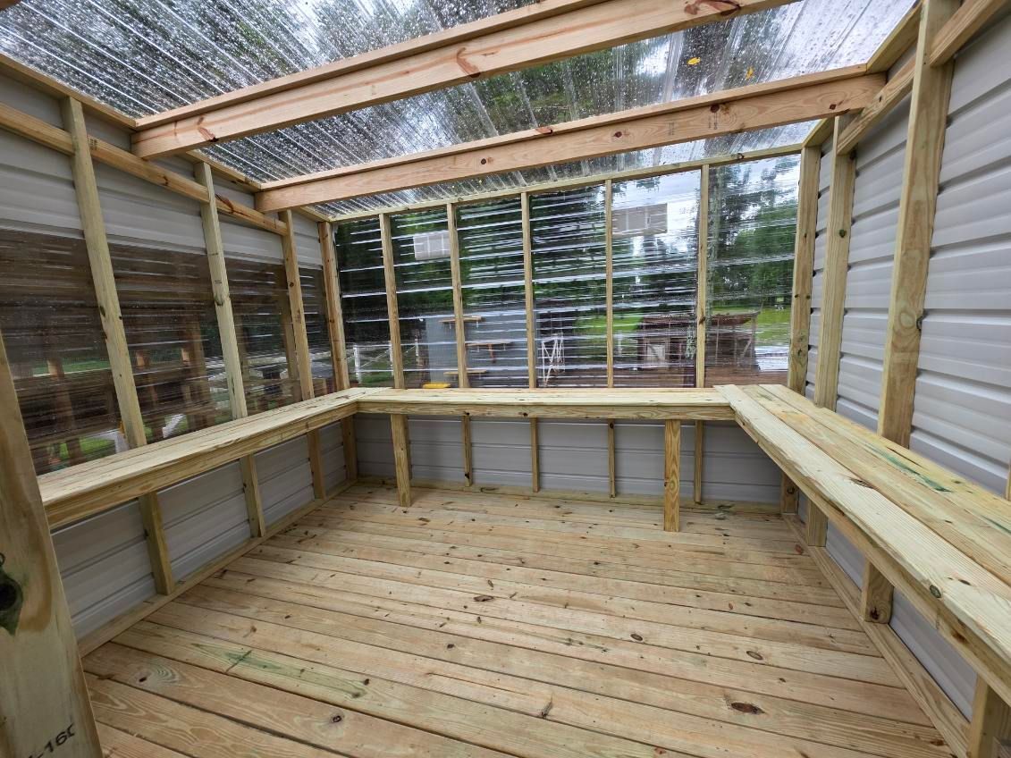 Wooden screened-in porch with a slatted deck, bench seating, and a skylit roof.