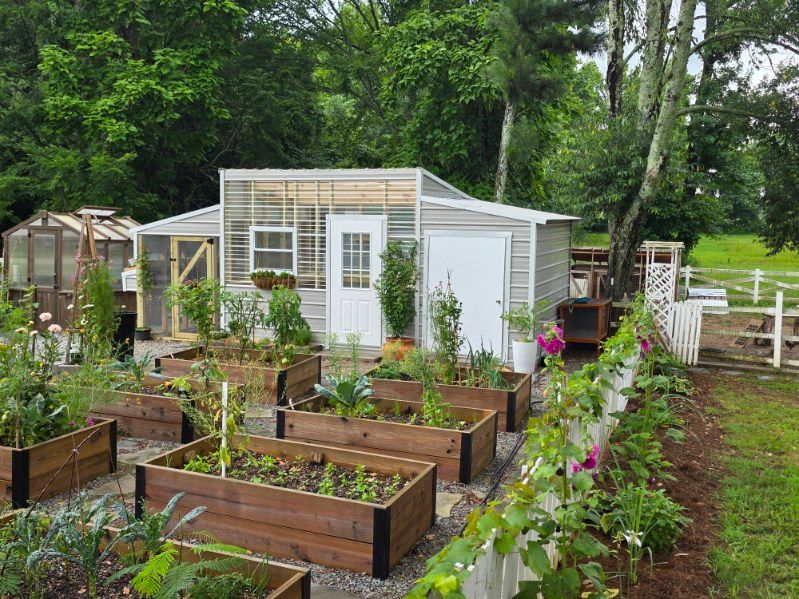 Small gray garden shed with white trim and double doors beside a lawn and tall ornamental grass.