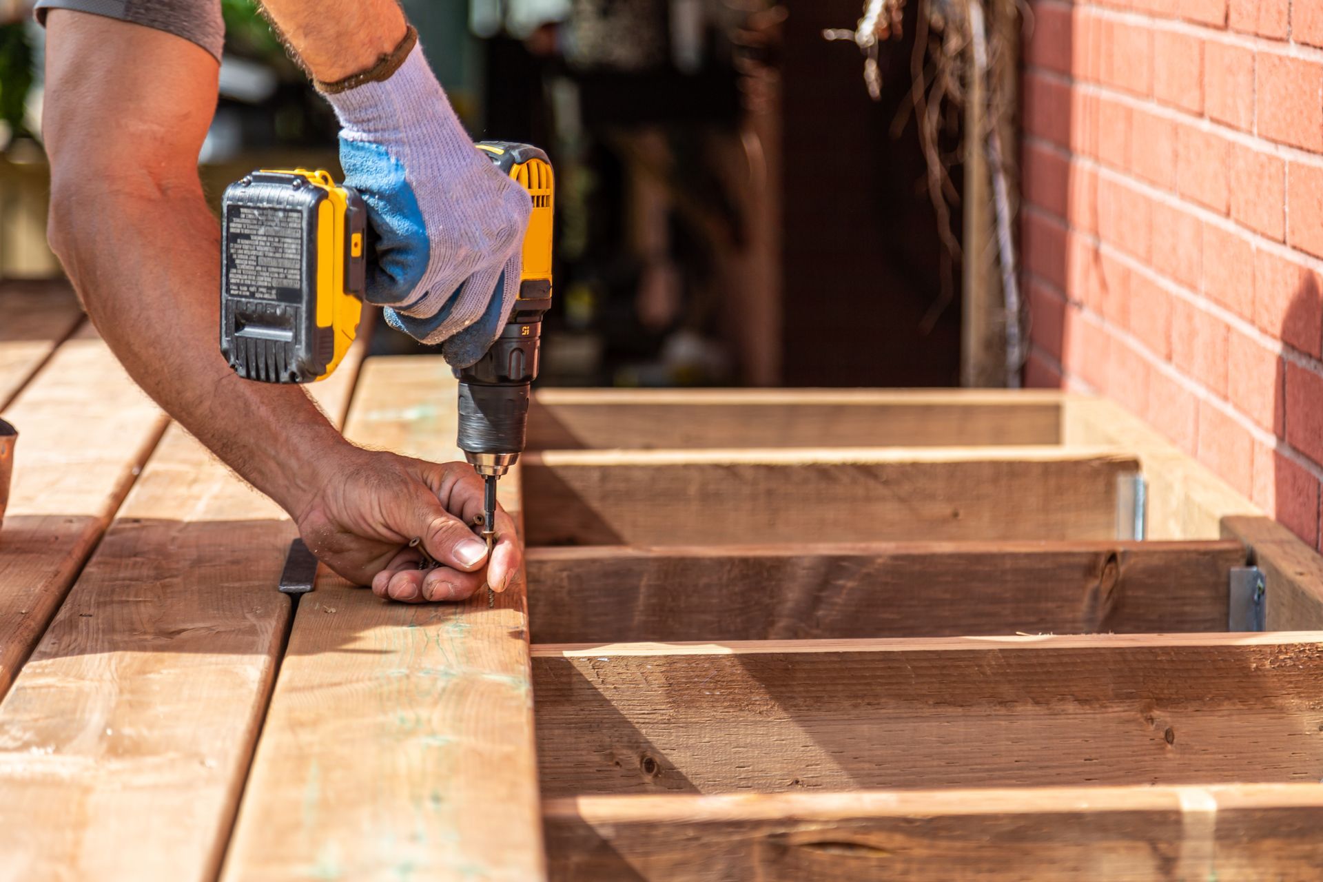 Worker using a drill to fasten wooden beams beside a brick wall