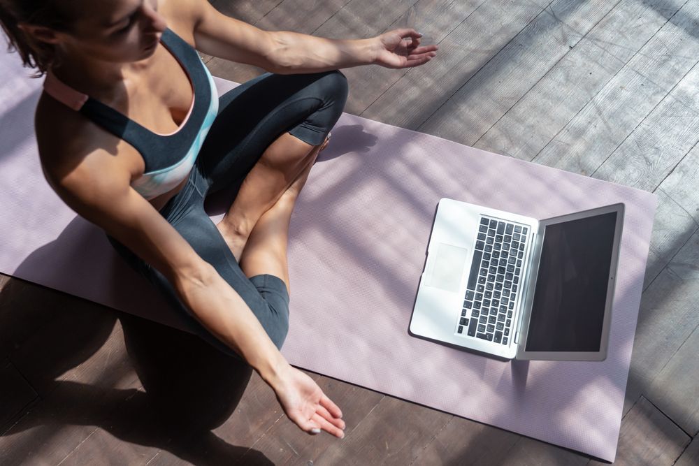 A Woman Is Sitting On A Yoga Mat Next To A Laptop — The Therapists Cairns In Cairns City, QLD