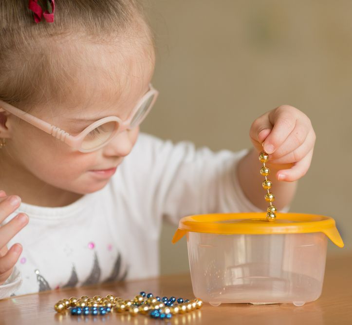 A Little Girl Wearing Glasses Is Playing With Beads In A Plastic Container — The Therapists Cairns In Cairns City, QLD