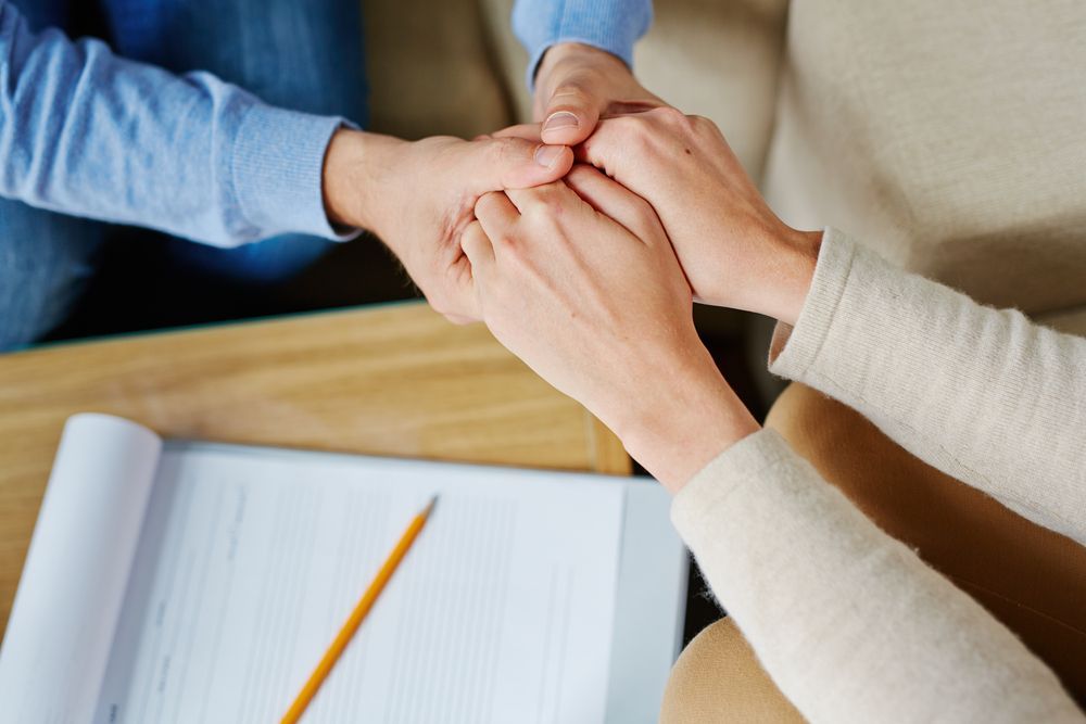 A Man And A Woman Are Holding Hands While Sitting At A Table — The Therapists Cairns In Cairns City, QLD