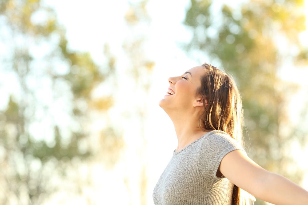 A Woman Is Laughing With Her Arms Outstretched In A Park — The Therapists Cairns In Cairns City, QLD