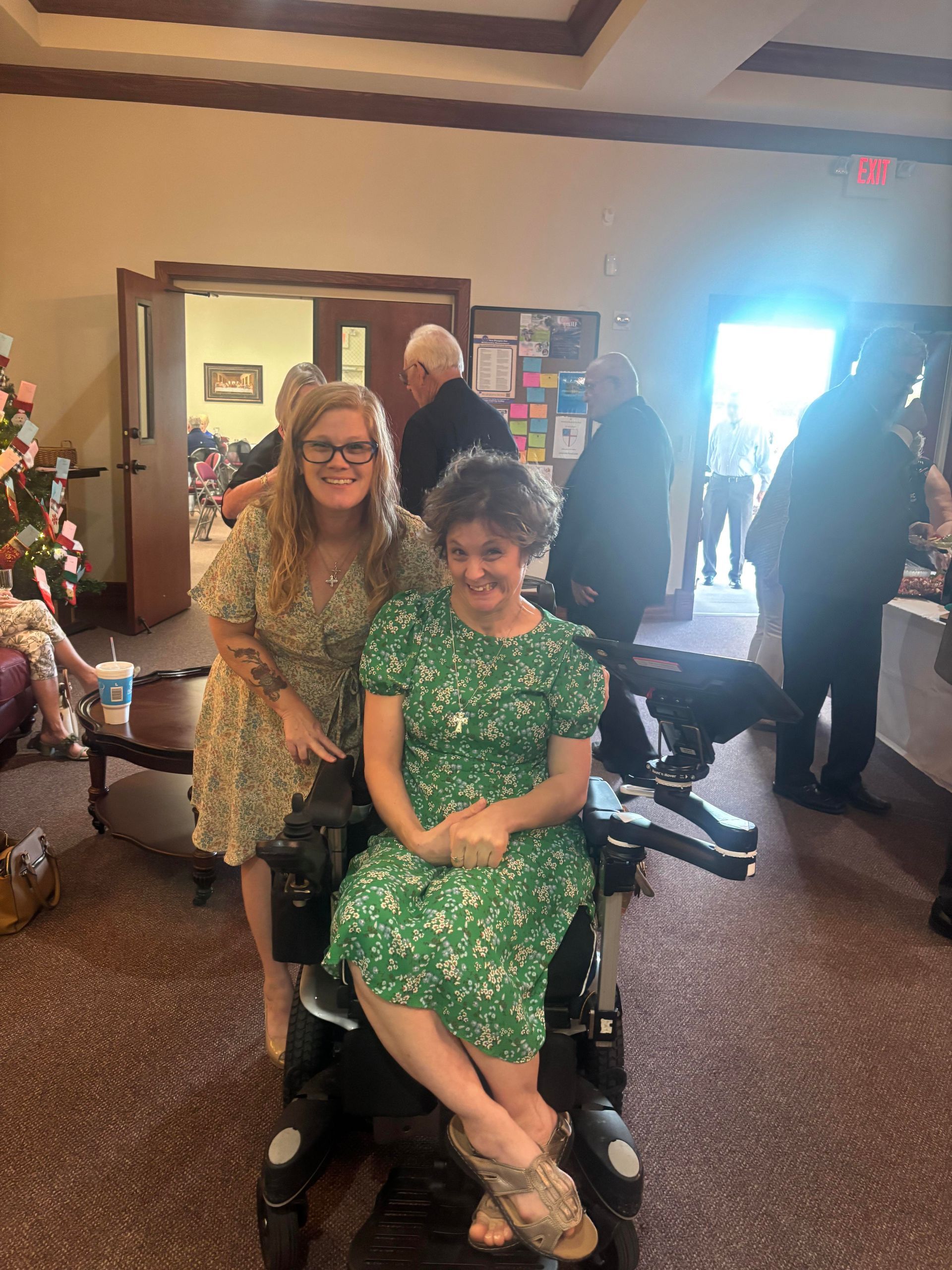 A woman in a green dress is sitting in a wheelchair next to another woman.