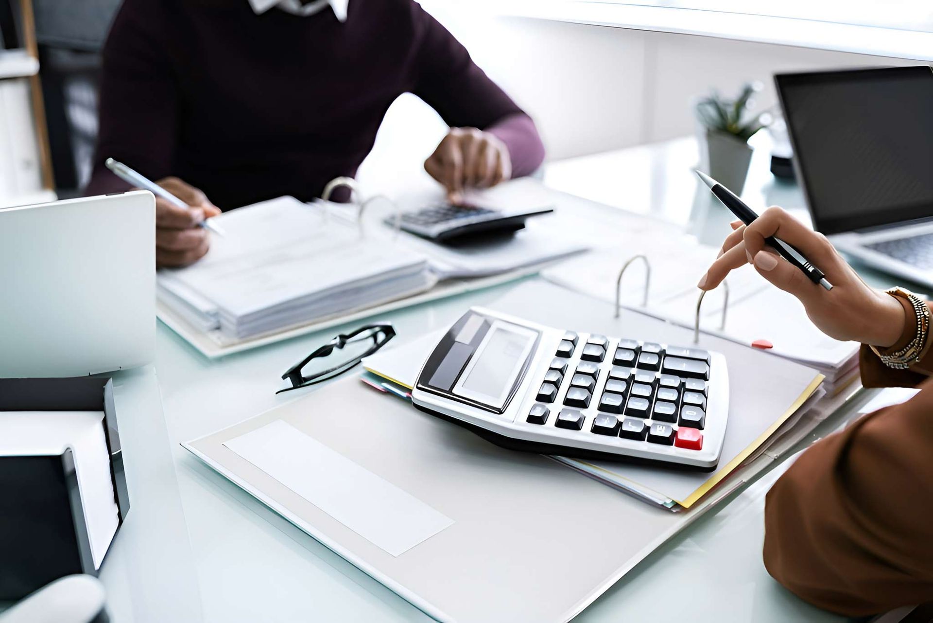 Two People Are Sitting At A Table With A Calculator And A Laptop — Dynamic Accounting Taxation Advisors in Terrigal, NSW