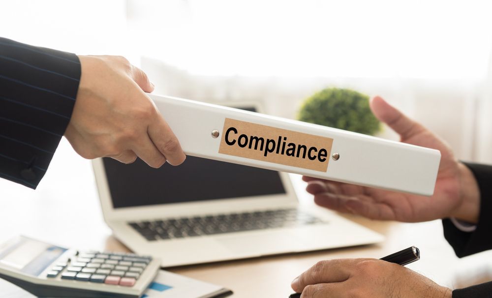 A Man Is Handing A Binder With The Word Compliance — Dynamic Accounting Taxation Advisors in Terrigal, NSW