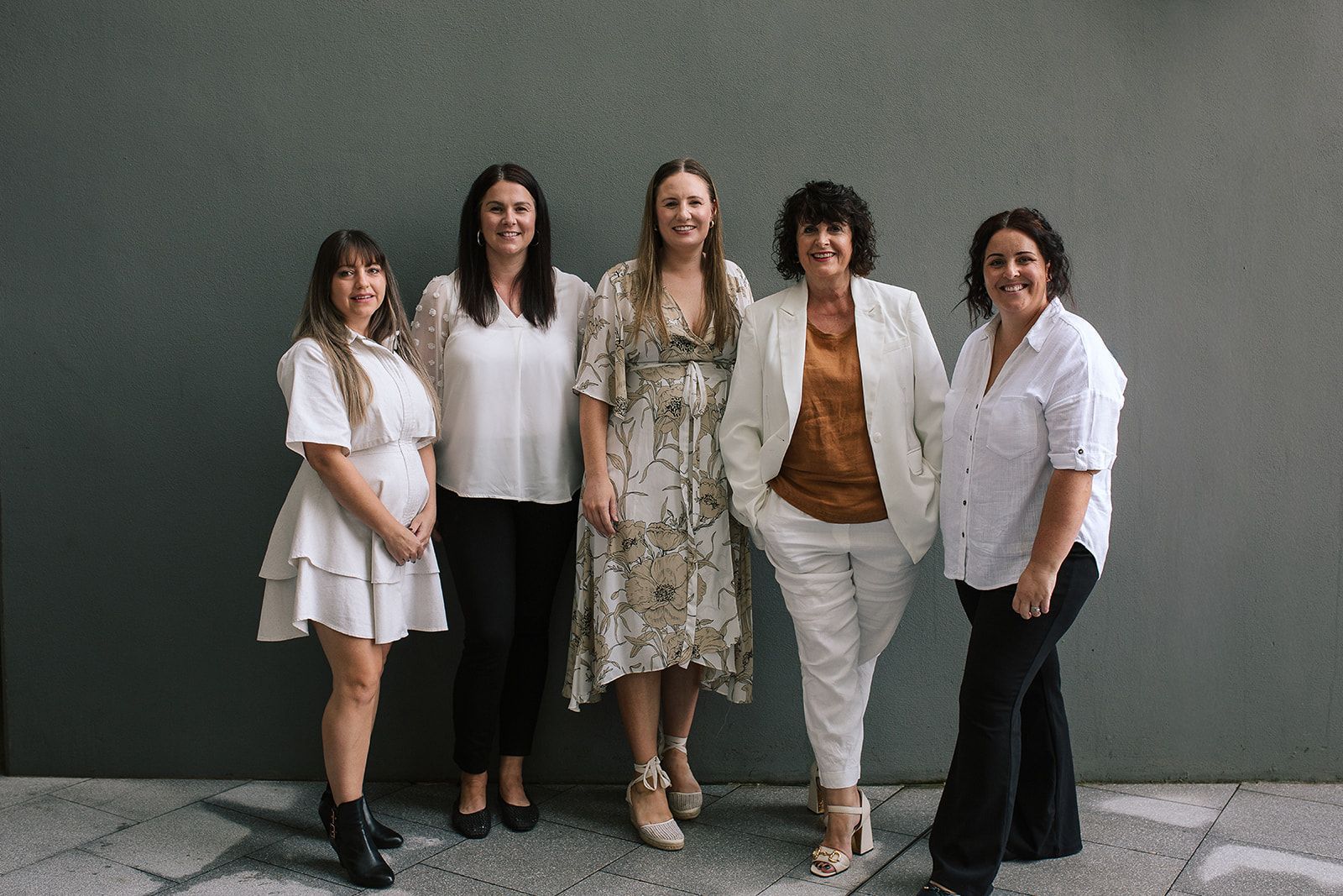 Five people standing together outdoors against a gray wall, smiling at the camera — Dynamic Accounting Taxation Advisors in Terrigal, NSW