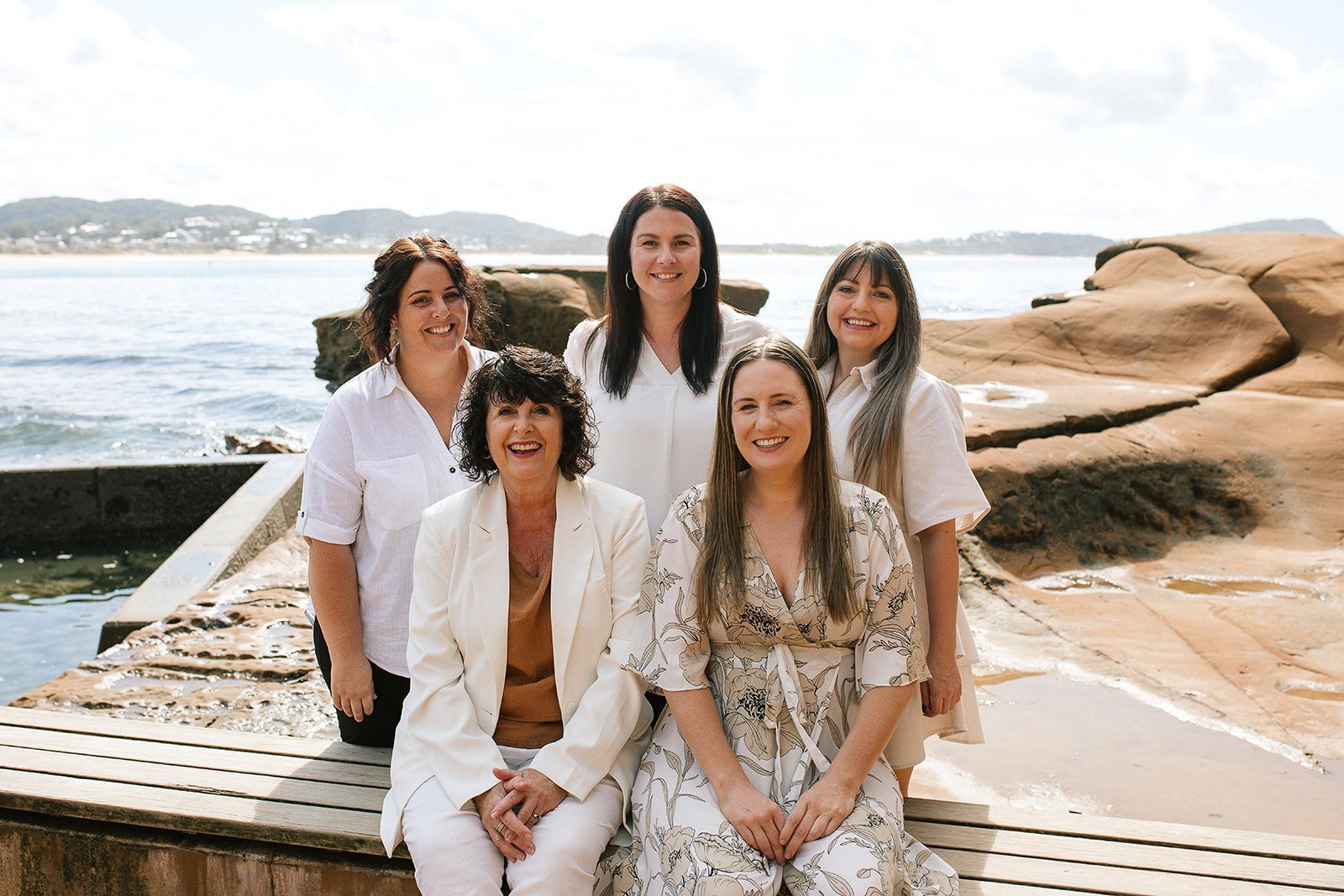 Five people pose on a seaside deck with rocks and water in the background — Dynamic Accounting Taxation Advisors in Terrigal, NSW