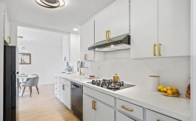 A kitchen with white cabinets and gold handles and a stove top oven.
