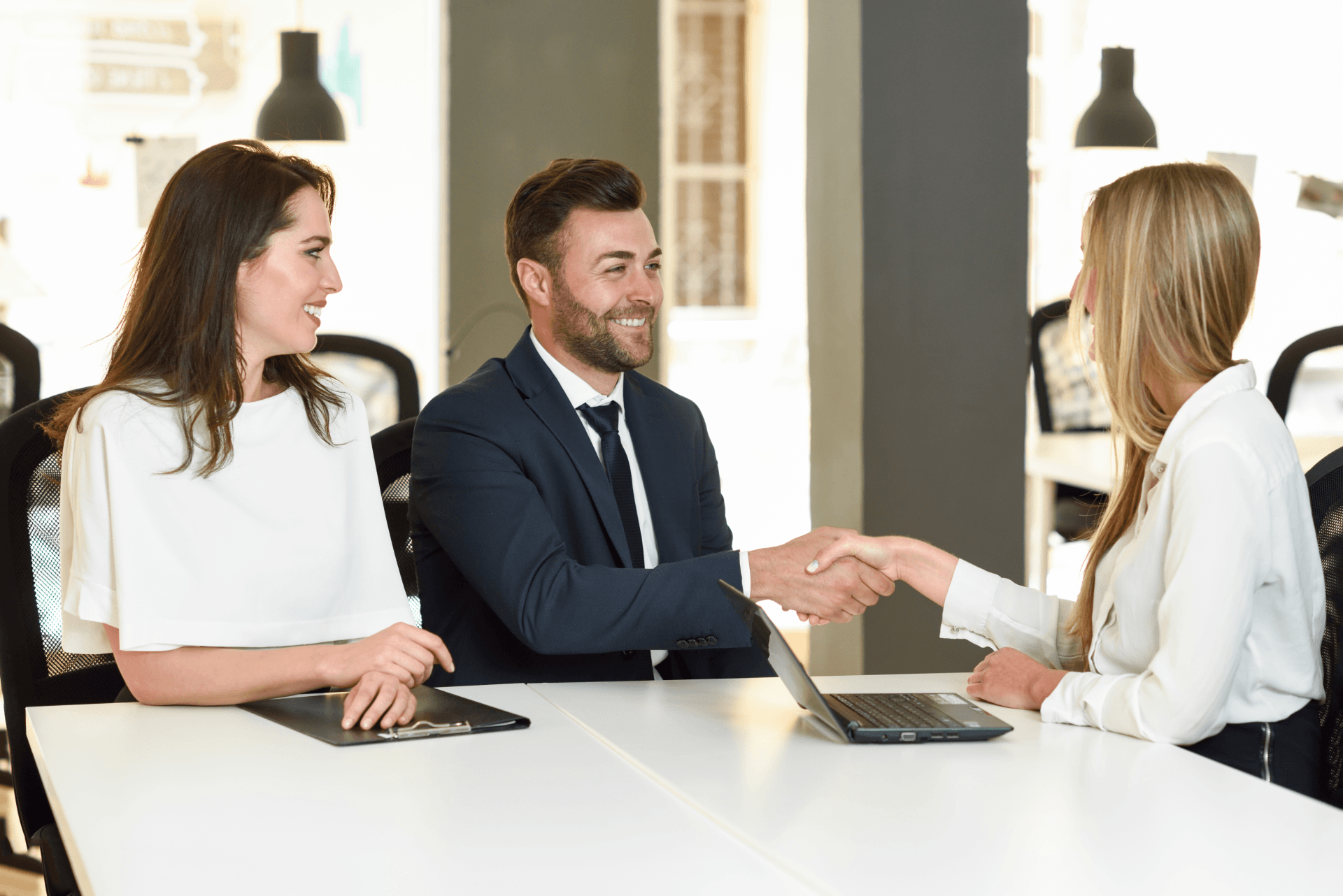 A man and a woman are shaking hands while sitting at a table.