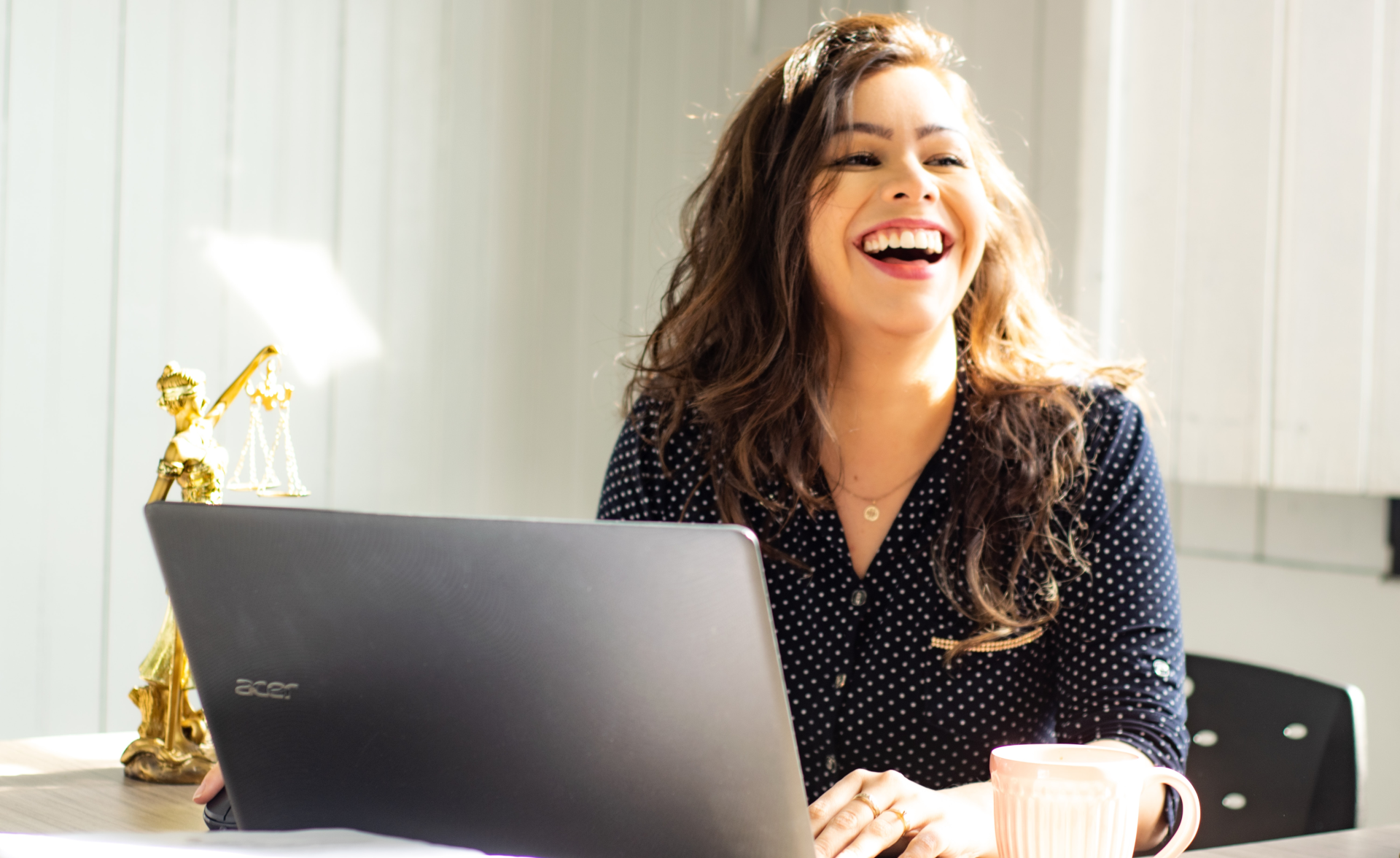 A woman is sitting at a table with a laptop and laughing.