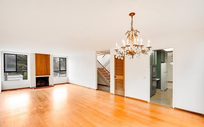 An empty living room with hardwood floors and a chandelier hanging from the ceiling.