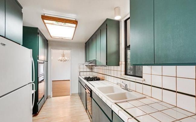 A kitchen with green cabinets and white tile counter tops
