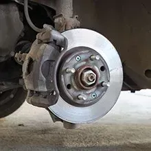 A vehicle's front disc brake assembly, showing the brake rotor, caliper, and wheel hub with lug studs.