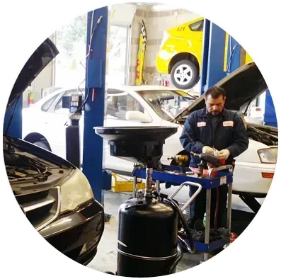 A mechanic in a blue uniform working at a car repair shop with an oil drain tank in the foreground.
