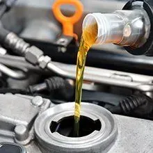 Golden motor oil being poured from a bottle into an open engine oil filler cap on a vehicle.