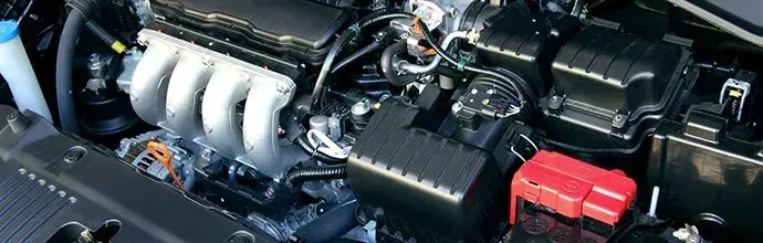 Engine bay of a vehicle showing an intake manifold, black plastic housing, and a red battery terminal cover.
