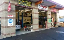 Exterior of a three-bay auto repair shop with open garage doors, concrete block walls, and an American flag.