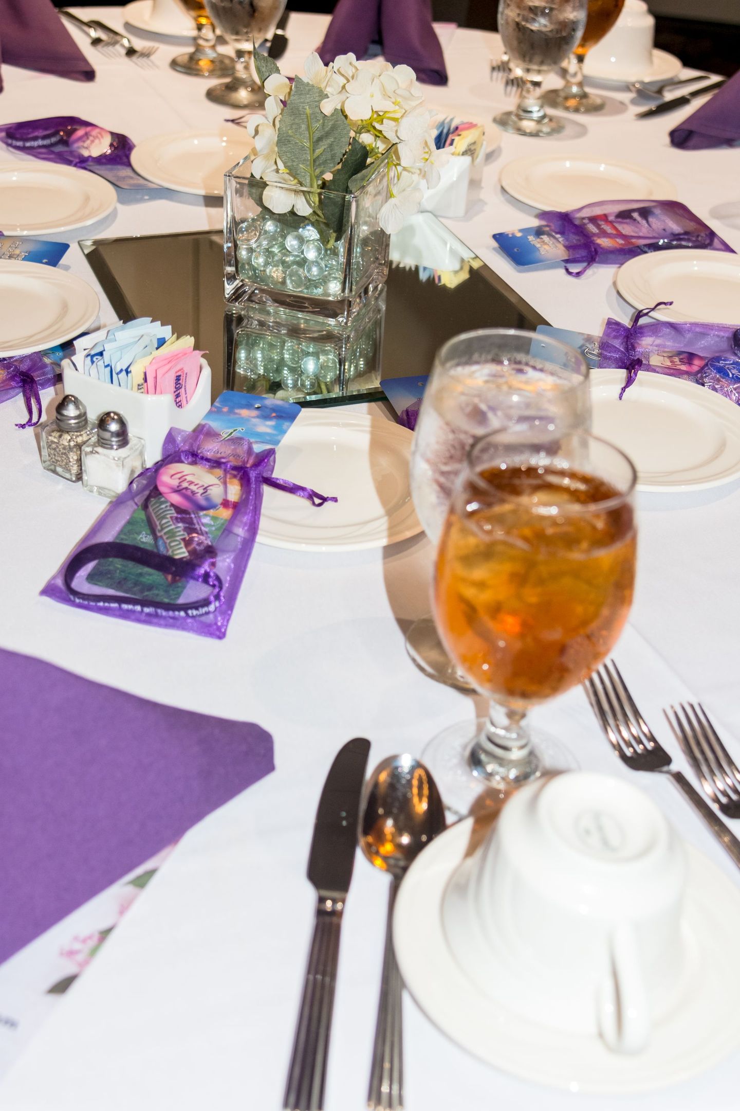 Purple-themed banquet table set with white plates, flowers, and iced tea in a glass.