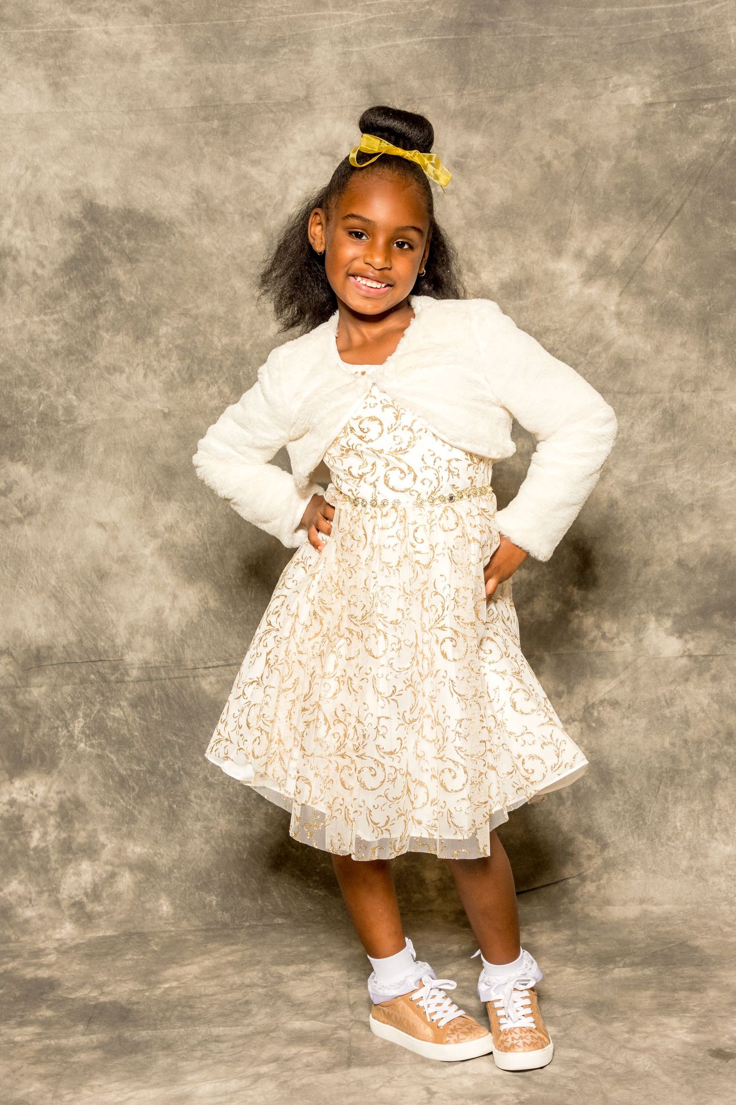 Child posing with hands on hips in a white sweater and floral skirt against a gray studio backdrop