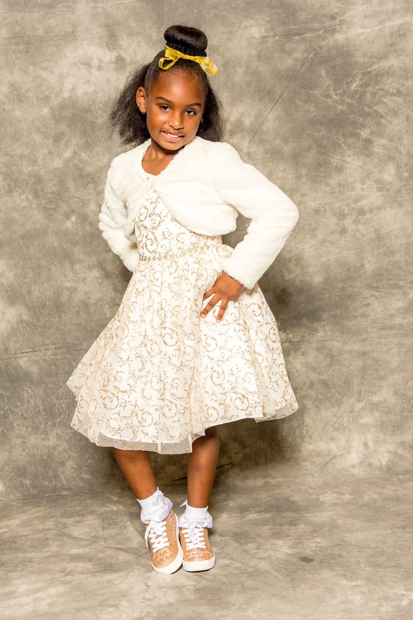 Child posing in a white floral dress and sneakers against a gray backdrop