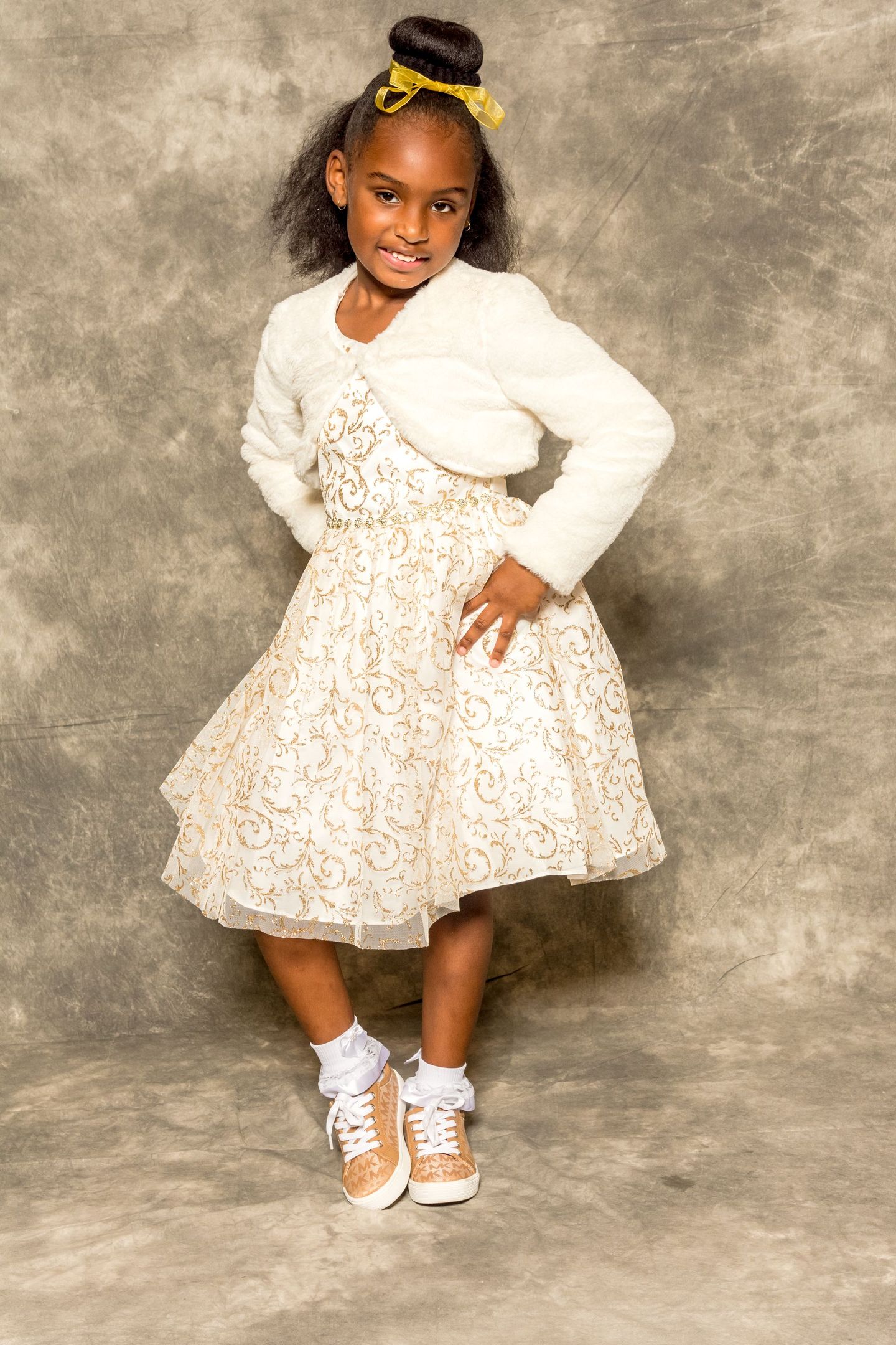 Young child in a cream dress posing against a neutral studio backdrop