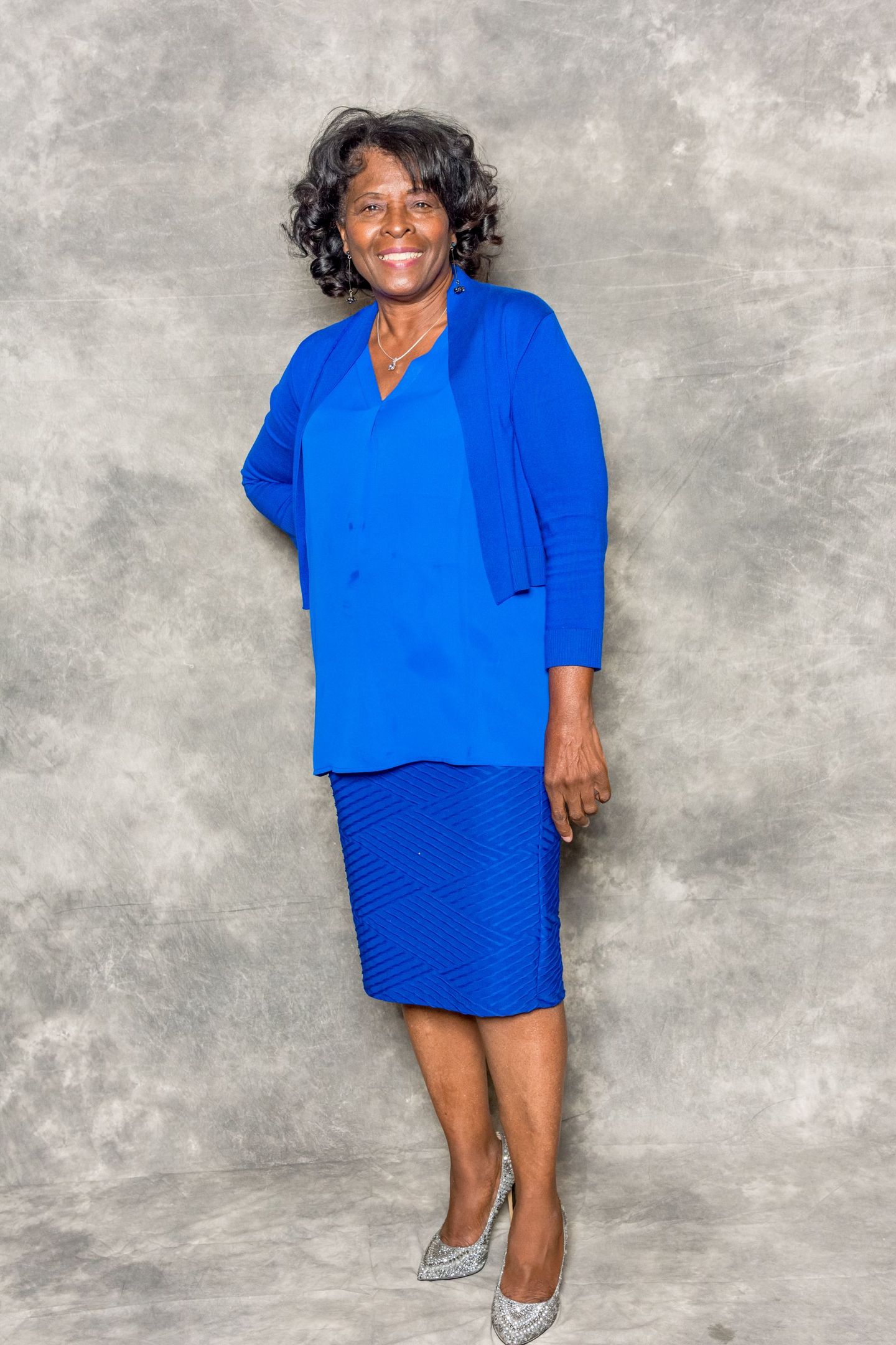 Woman in a bright blue suit standing against a gray backdrop, smiling.