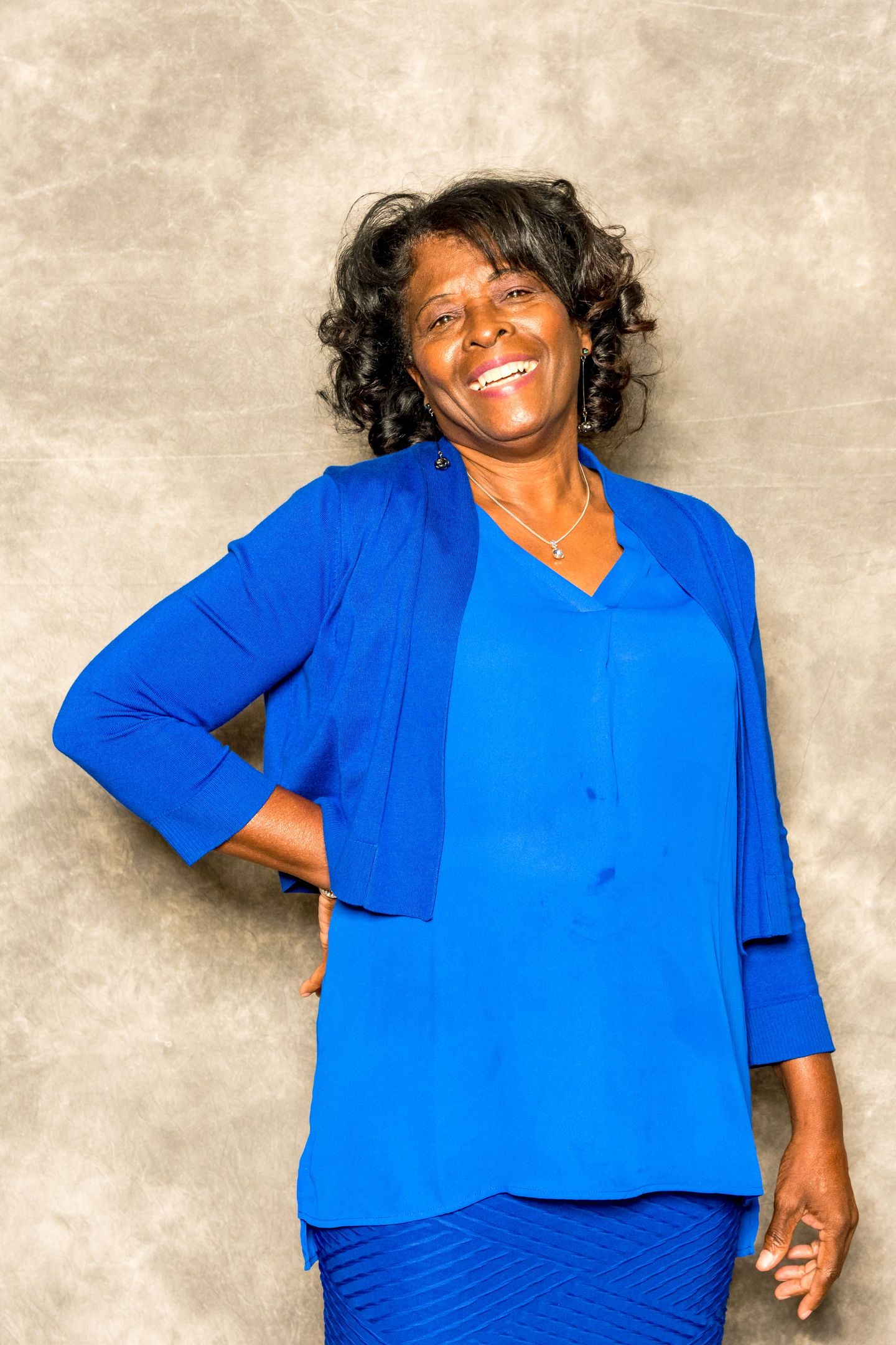 Smiling woman in a bright blue outfit, standing against a beige backdrop.