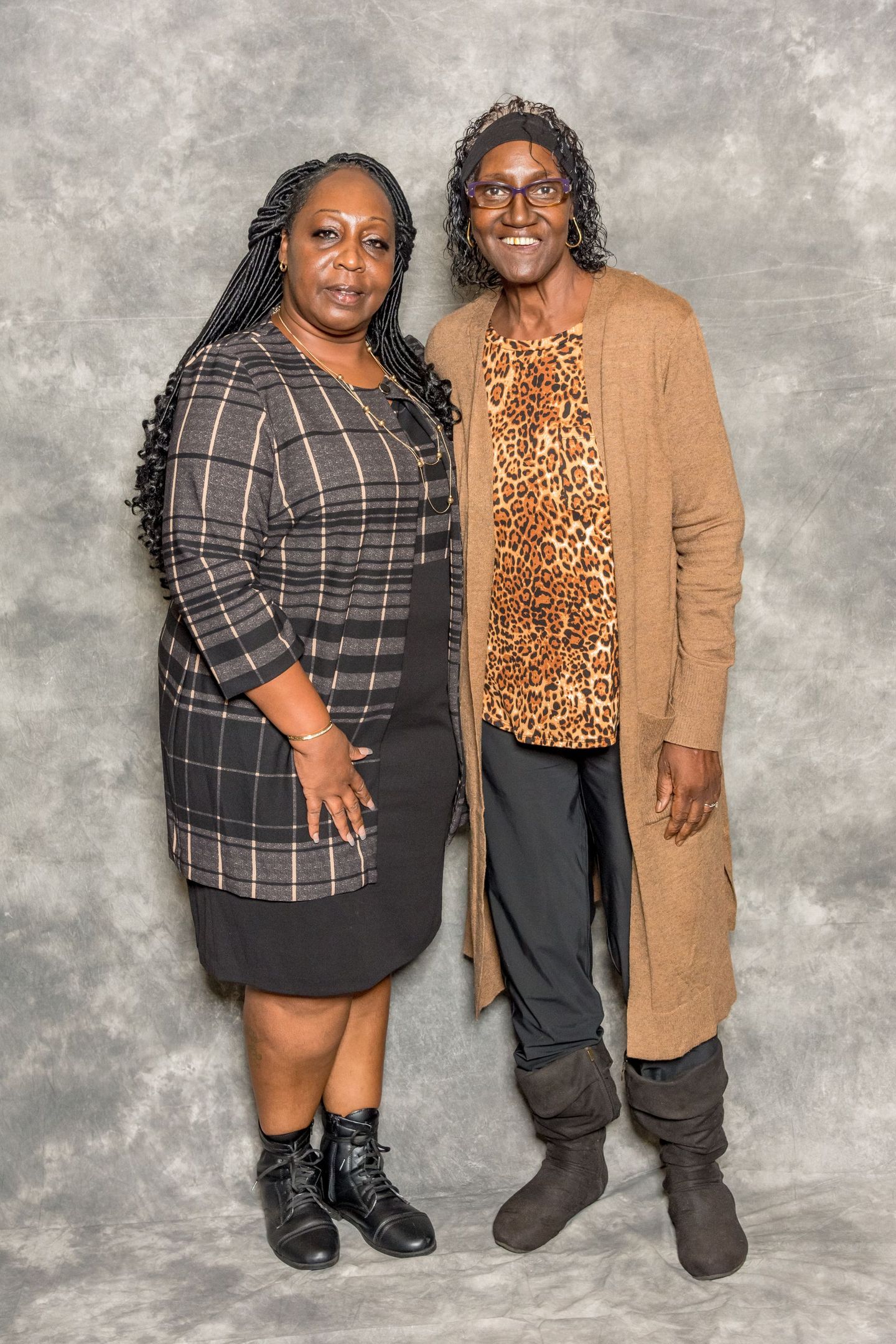 Two people standing side by side against a gray backdrop, wearing patterned outfits and black boots.