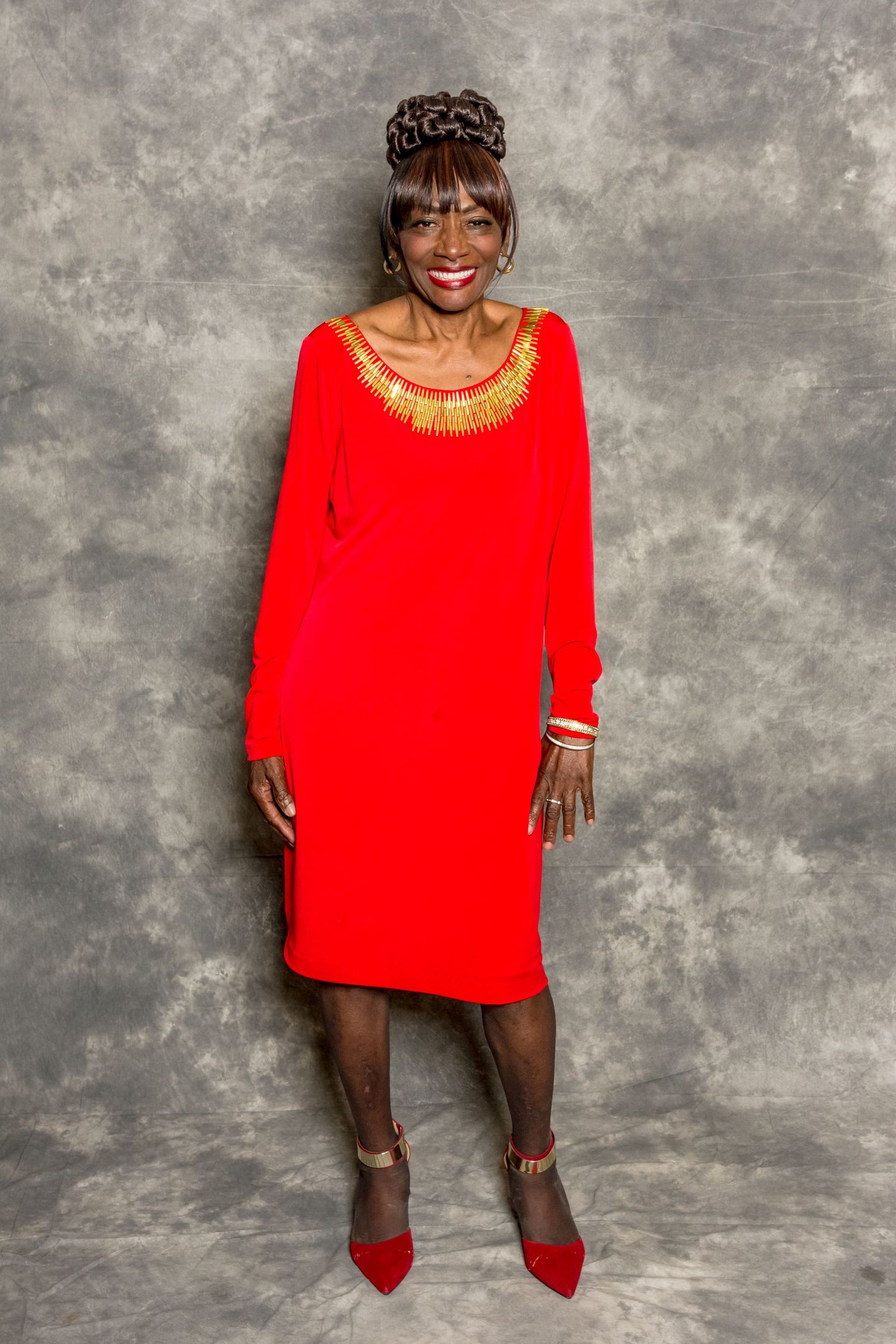 Woman in bright red dress and heels standing against a gray studio backdrop.