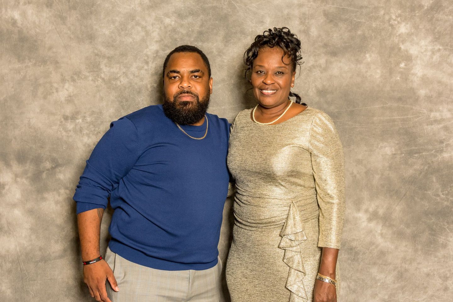 Two people posing together in front of a mottled gray backdrop, both smiling.