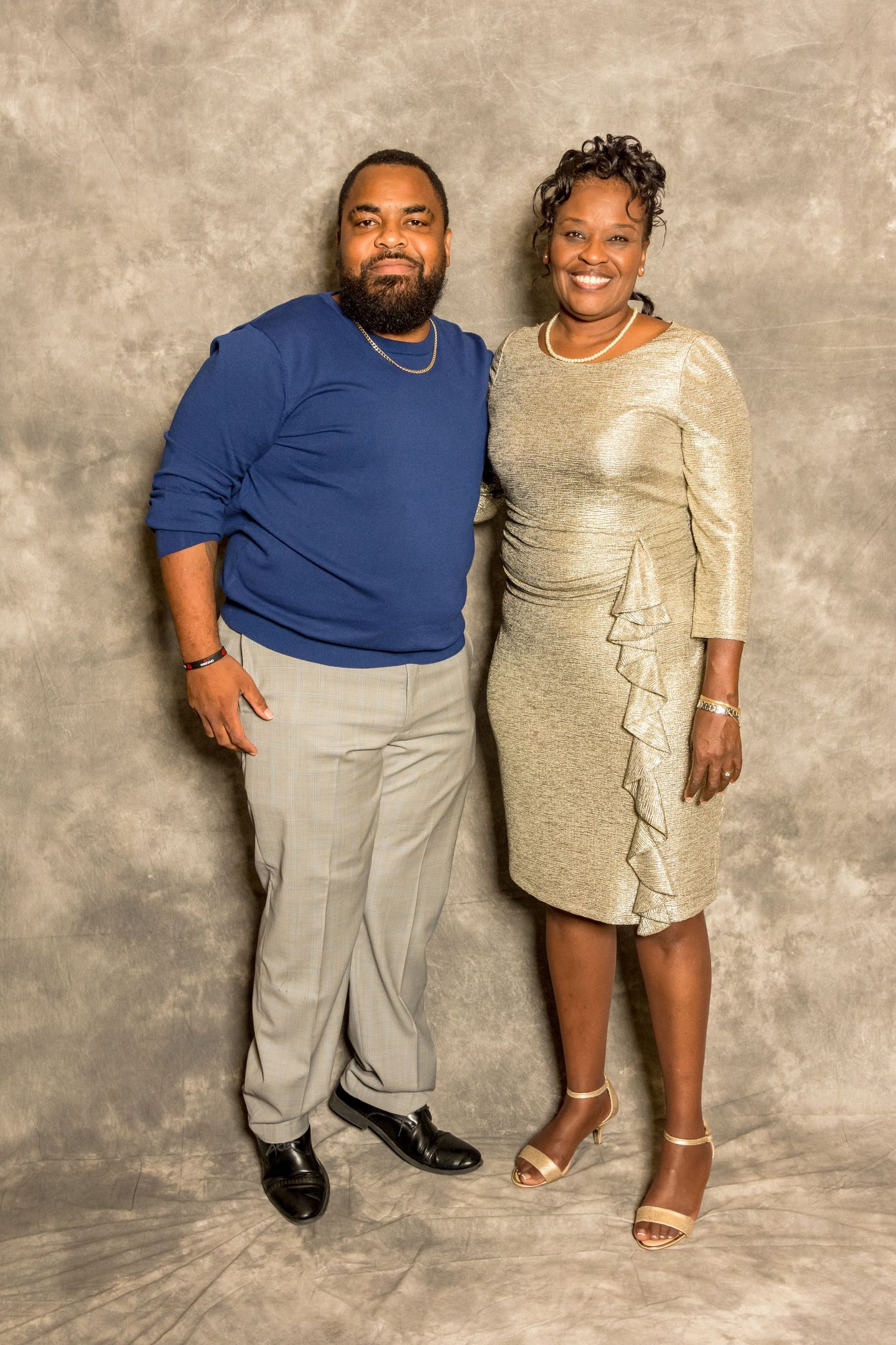 Two people posing together in front of a gray backdrop, both smiling and dressed in formal attire.