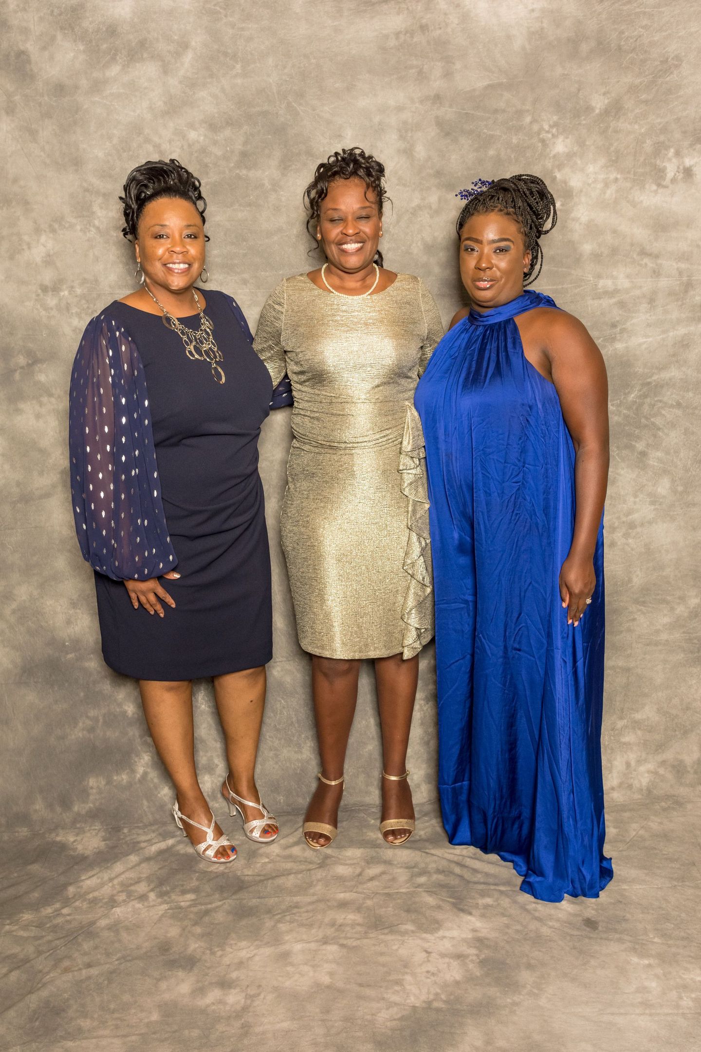 Three people posing in formal dresses against a gray studio backdrop.