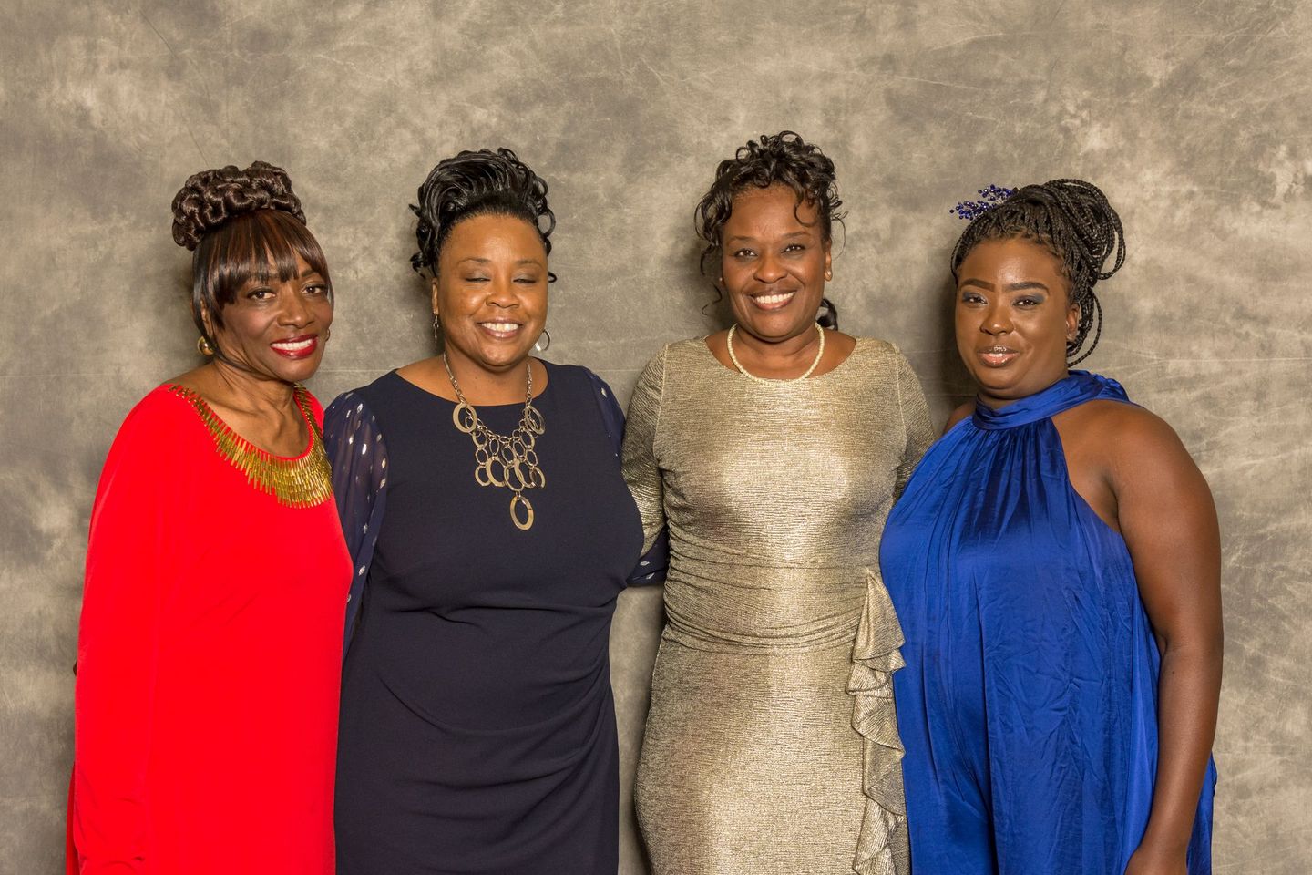 Four people posing together in formal dresses against a textured backdrop.