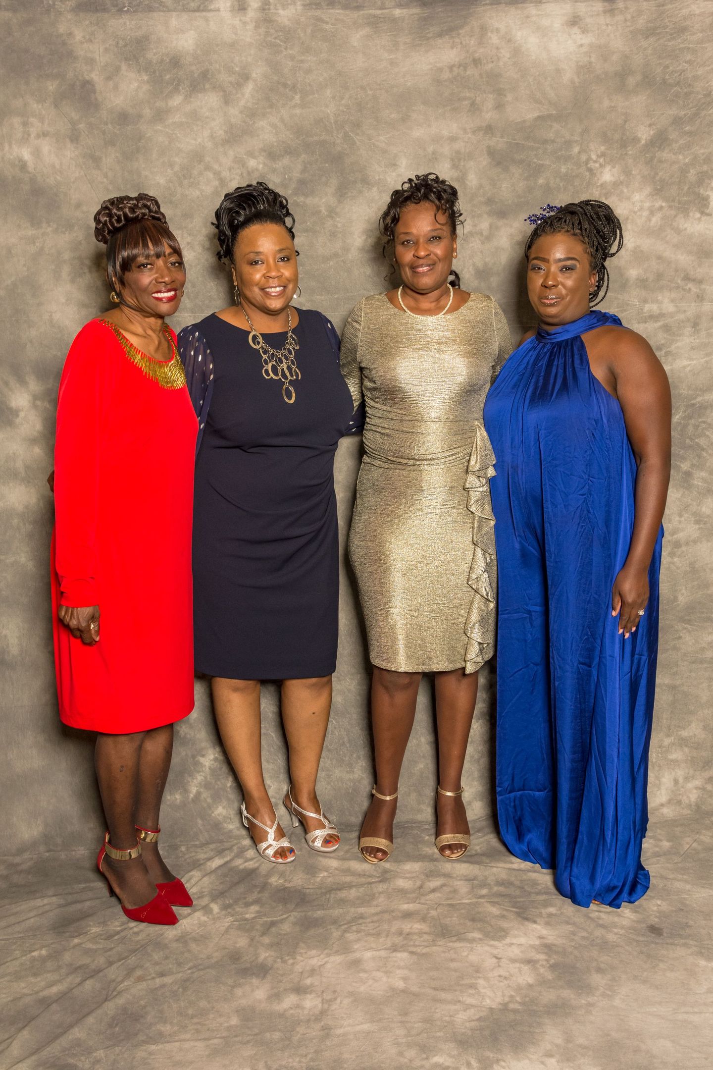 Four women posing in formal dresses against a neutral backdrop