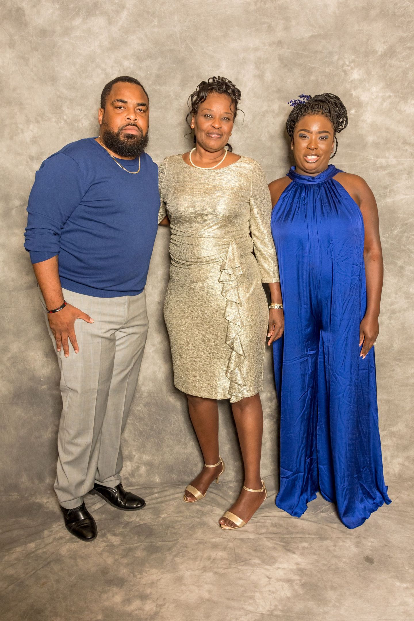 Three people posing together against a beige backdrop, dressed in formal attire.