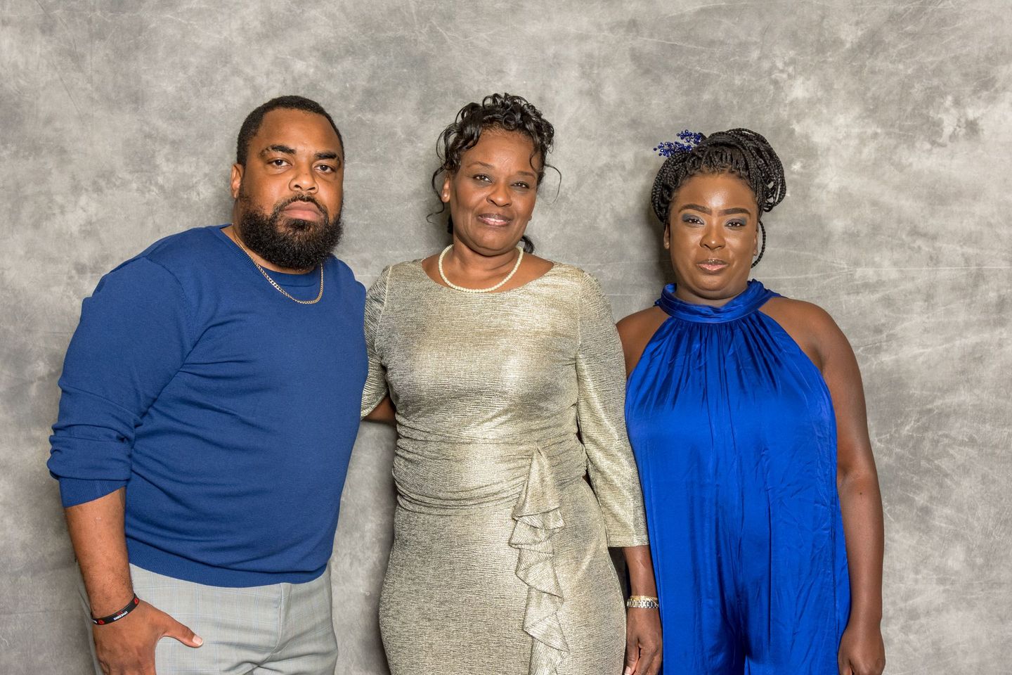 Three people posing against a gray backdrop, wearing blue and silver outfits.