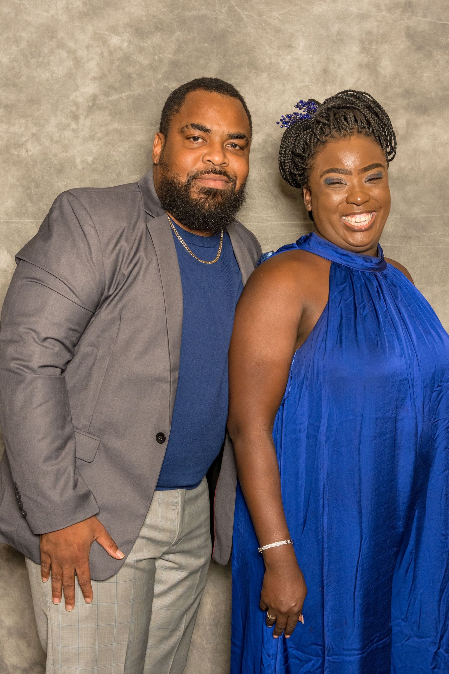 Two people posing together in front of a gray backdrop, smiling in formal attire