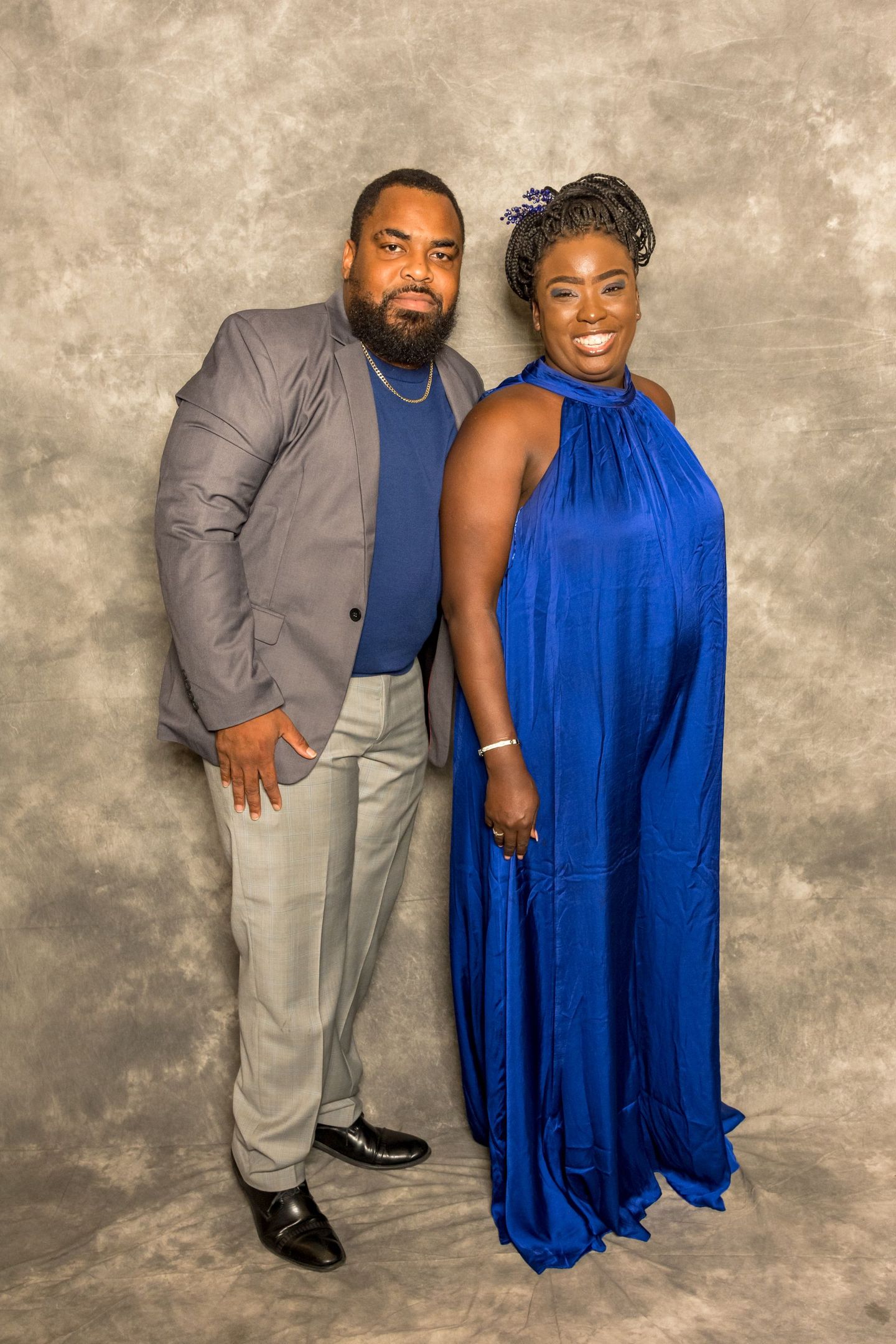 Two people standing against a gray backdrop, dressed in formal attire, smiling at the camera.