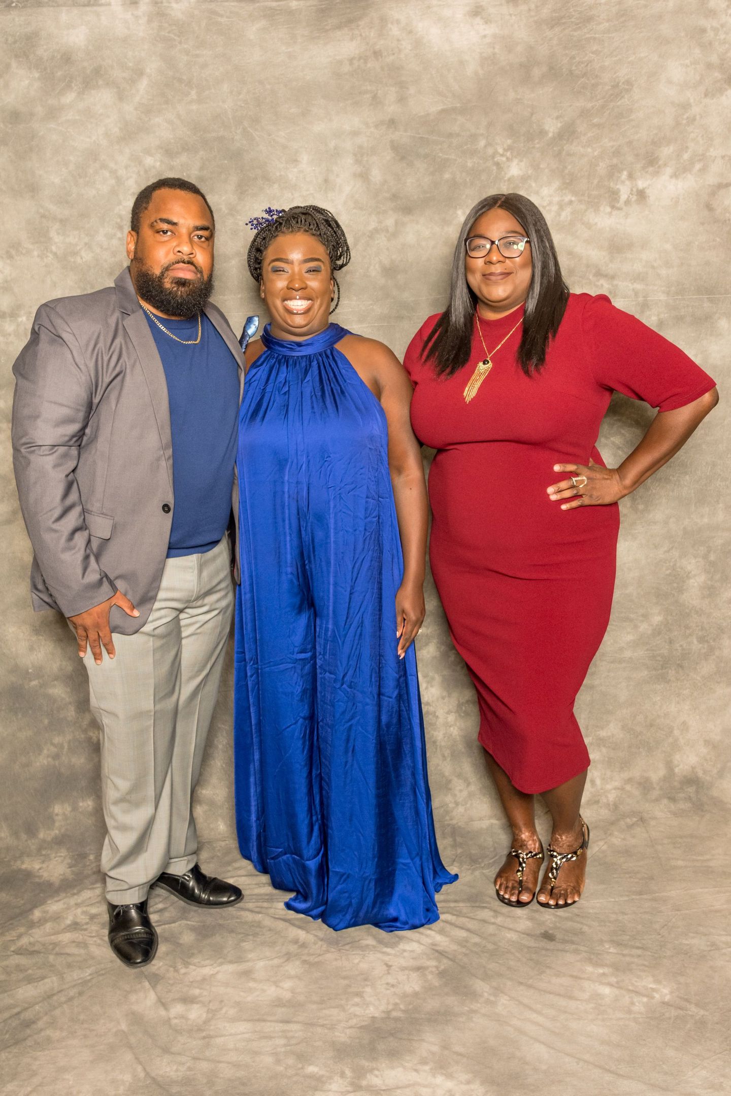 Three people posing together against a mottled studio backdrop, wearing gray, blue, and red outfits.