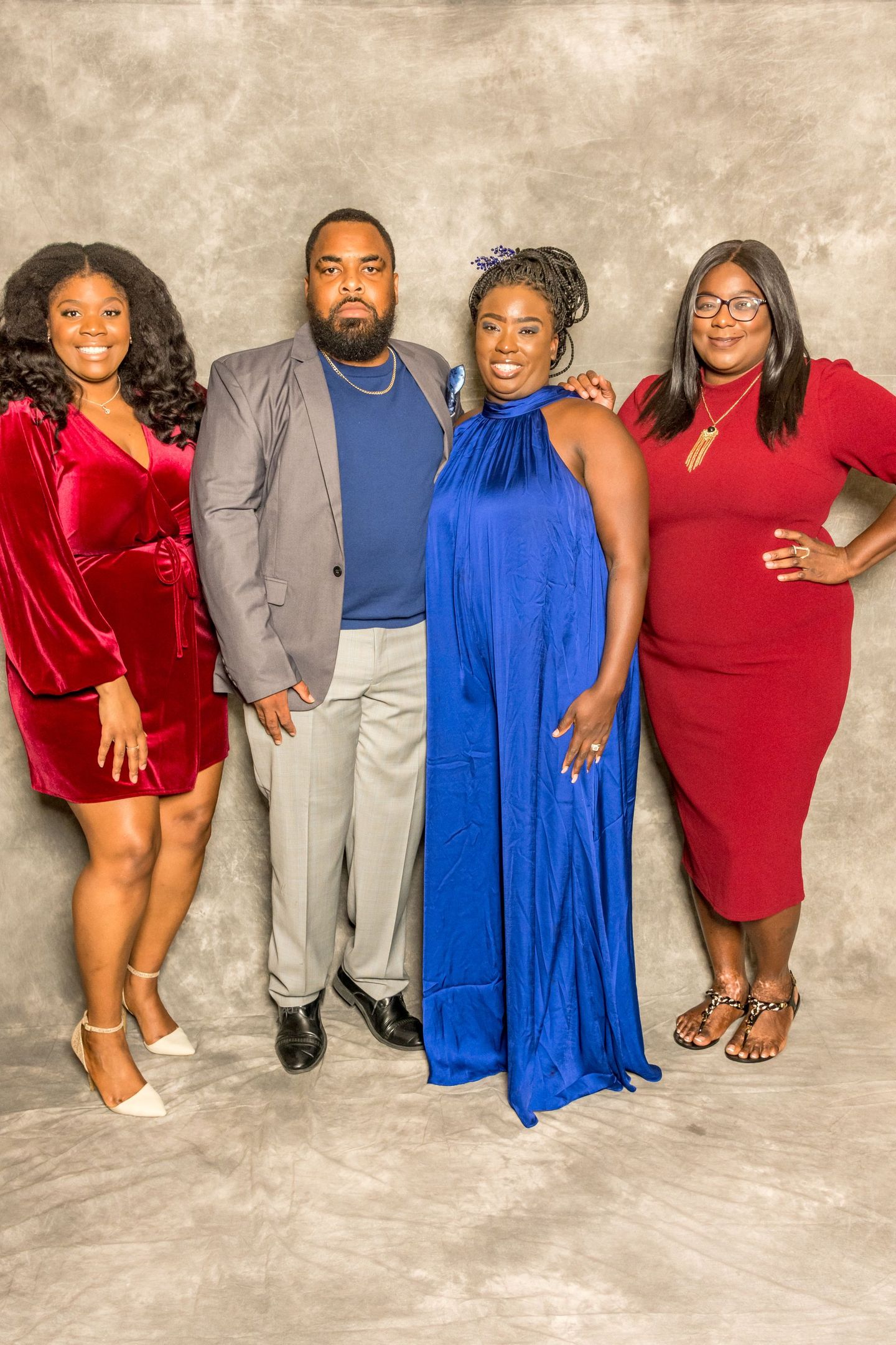 Four people pose together in formal attire against a beige studio backdrop.