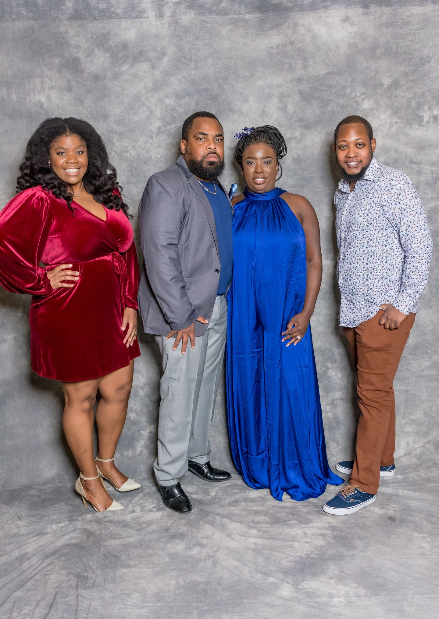 Four people posing on a gray backdrop, wearing red, gray, blue, and patterned outfits.