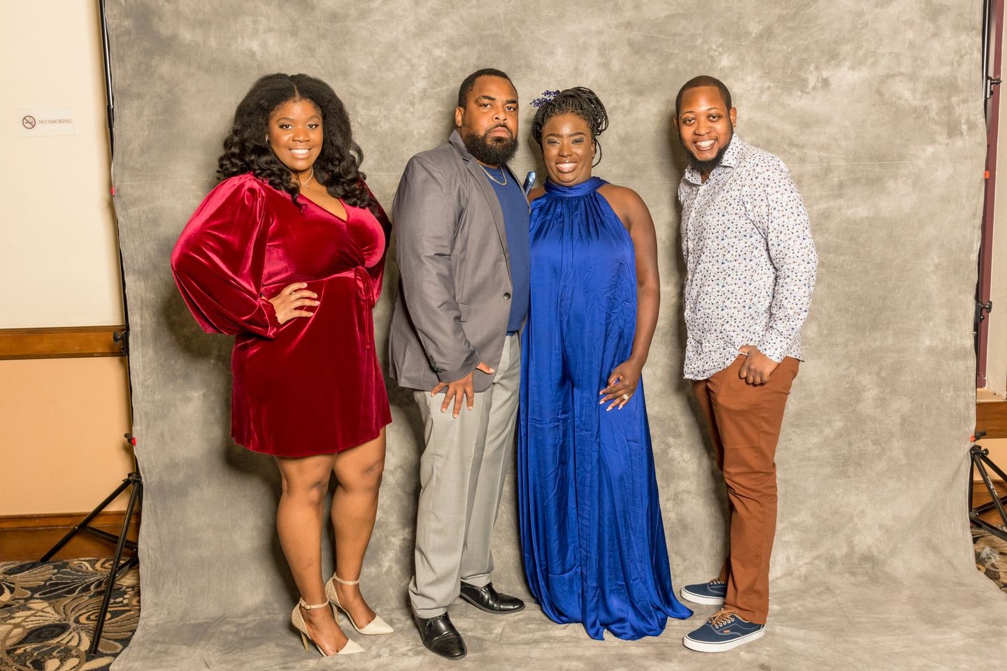 Four people posing in formal outfits in front of a gray backdrop, smiling at the camera.